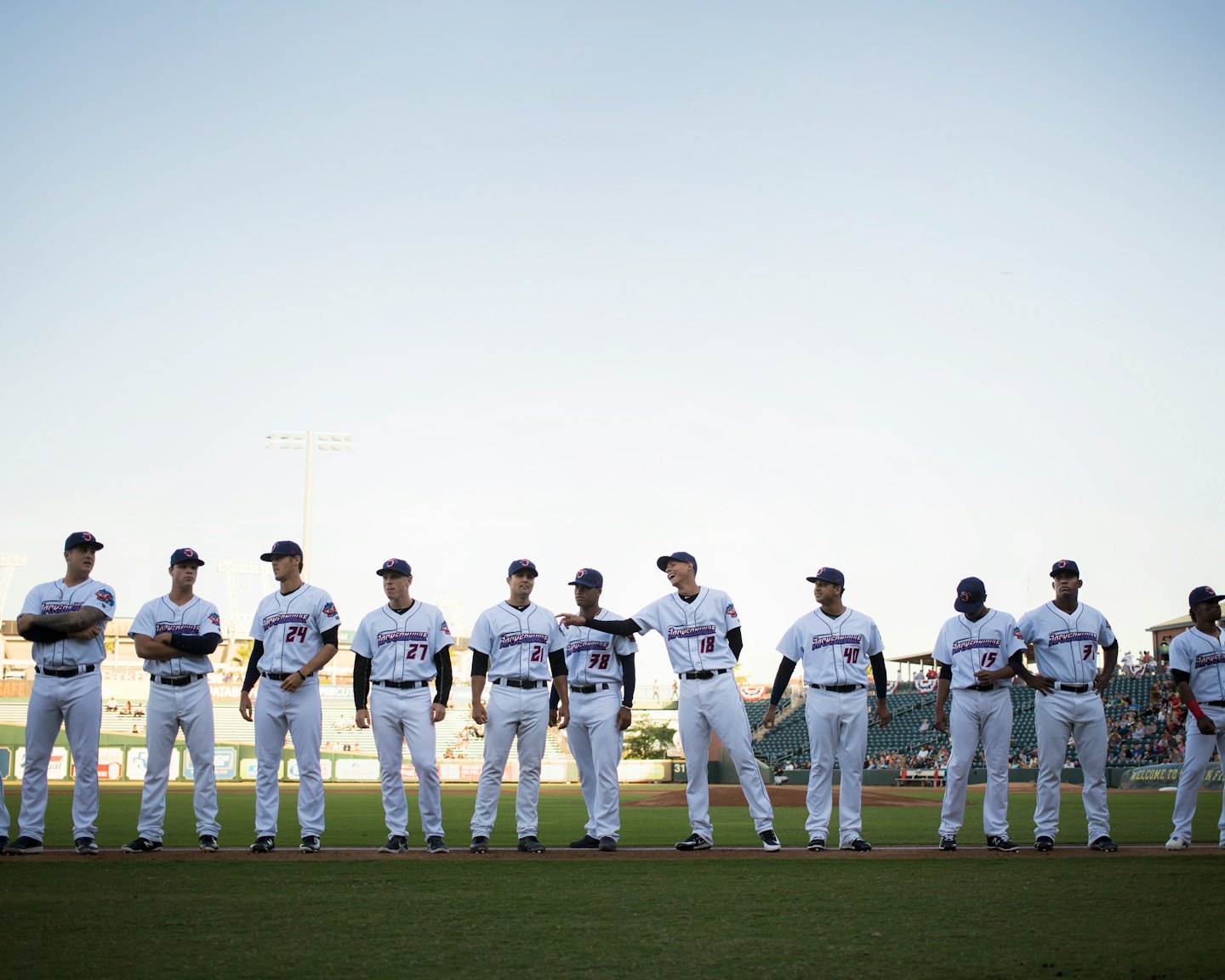 Baseball players in uniform on field under stadium lights.