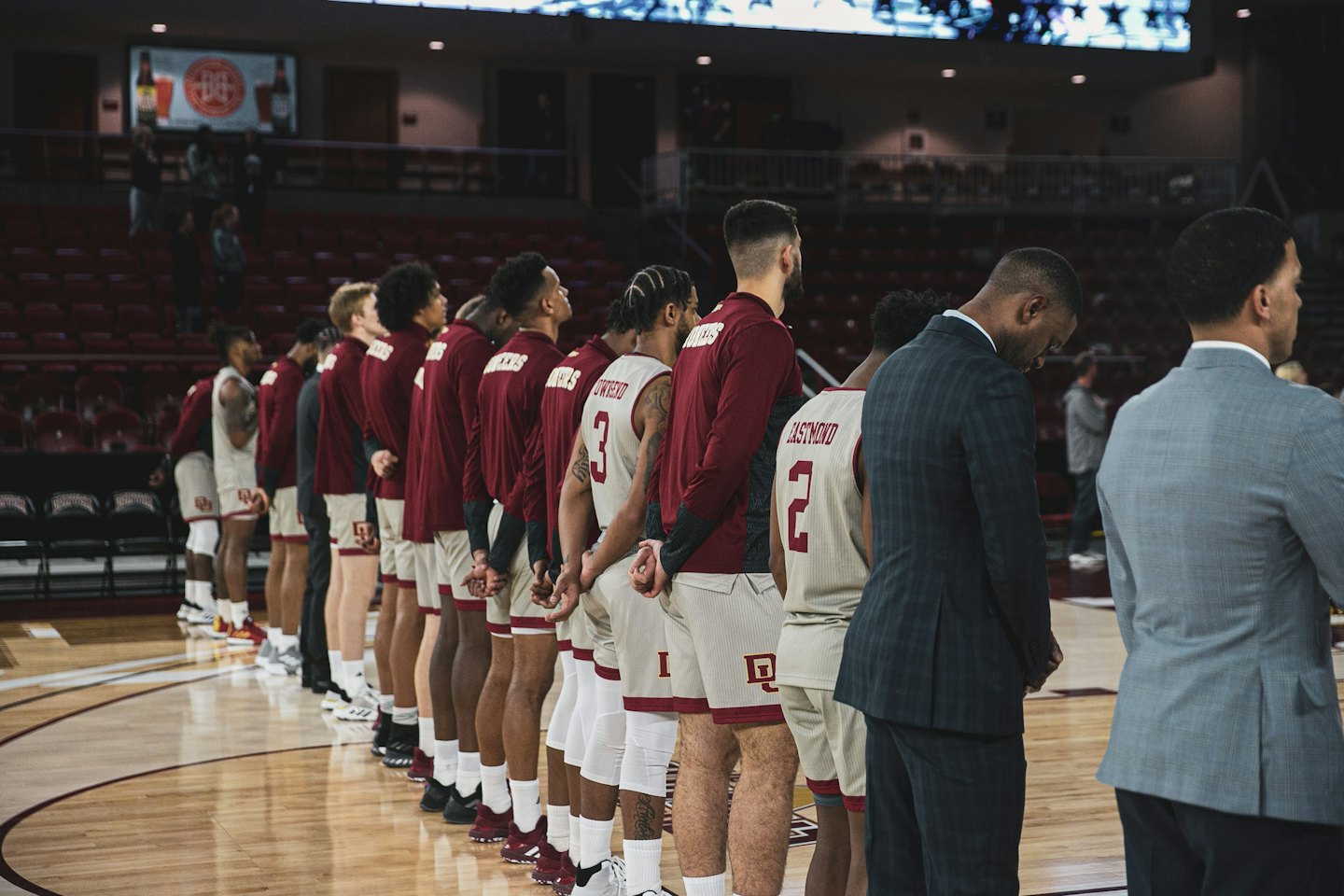 Basketball players and coaches stand in line on a court.